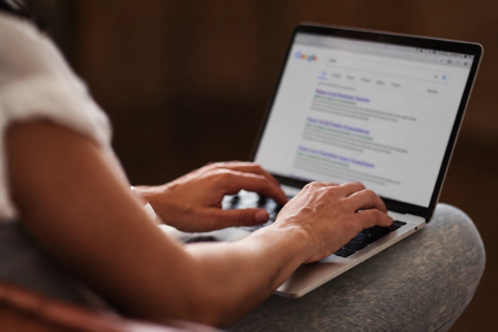 A person types a Google search on a laptop