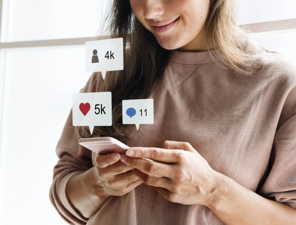 A woman smiles at a phone while follower, like and comment counts float beside her